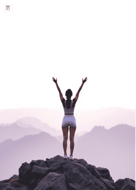 אישה עומדת על פסגת הר עם ידיים מונפות באוויר לניצחון, מסמלת את החופש שמגיע לאחר שינוי דפוסי חשיבה מגבילים.